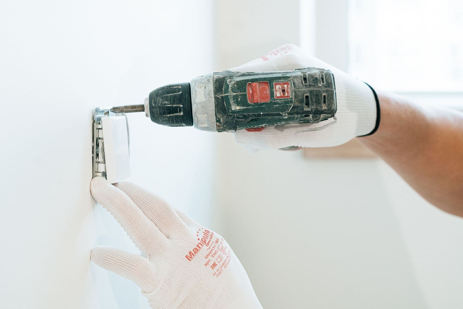 Electrician fastening a wall socket with a drill